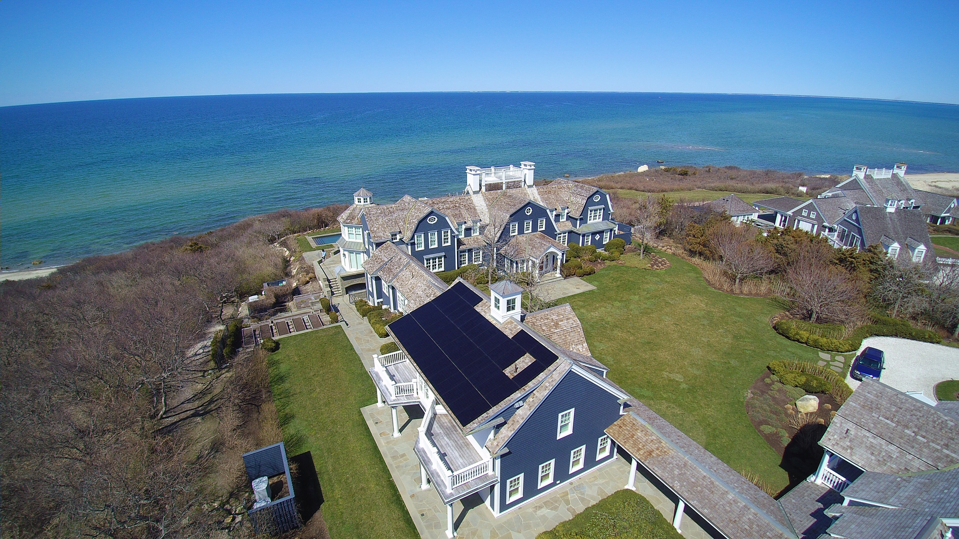 Vue aérienne d’une maison bleue en bord de mer, avec des panneaux solaires noirs installés sur un pan de toit.